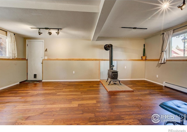 exercise room featuring a wood stove, rail lighting, a baseboard heating unit, a textured ceiling, and hardwood / wood-style flooring