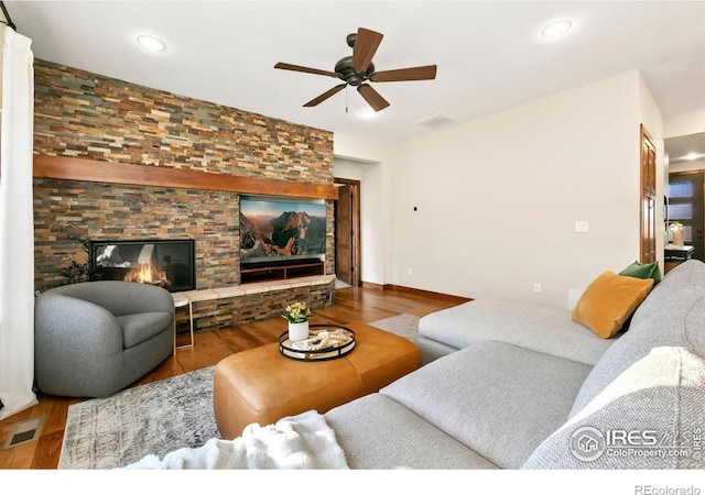 living room with ceiling fan, a stone fireplace, and hardwood / wood-style floors