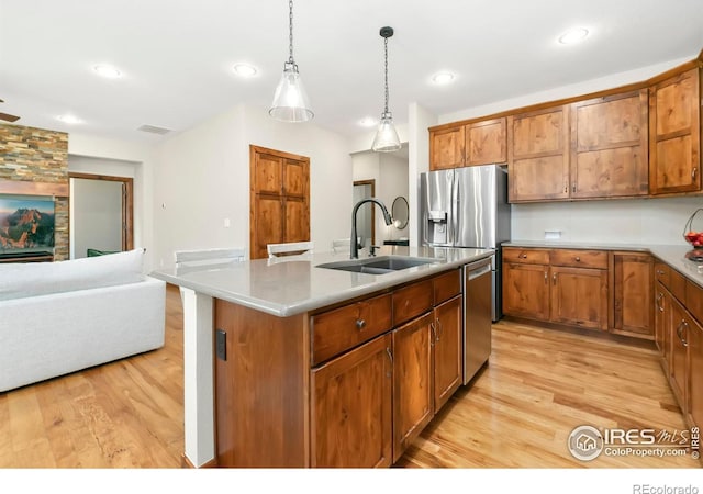 kitchen featuring sink, light wood-type flooring, decorative light fixtures, stainless steel dishwasher, and an island with sink