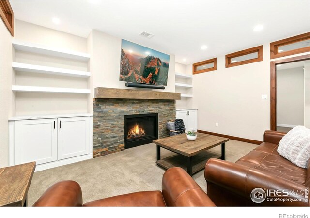 carpeted living room featuring a stone fireplace and built in shelves