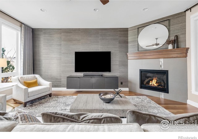 living room featuring light hardwood / wood-style floors, ceiling fan, and a tiled fireplace