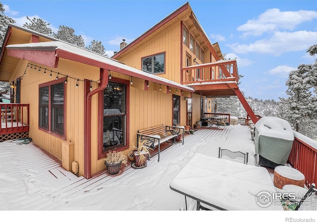 snow covered back of property featuring a balcony and a deck