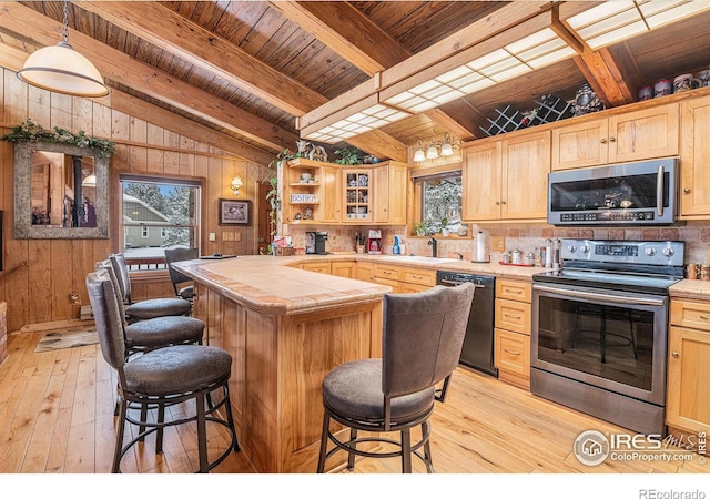 kitchen with light wood-type flooring, stainless steel appliances, wooden walls, beam ceiling, and light brown cabinets