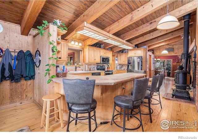 kitchen featuring beamed ceiling, appliances with stainless steel finishes, light hardwood / wood-style flooring, and wooden walls