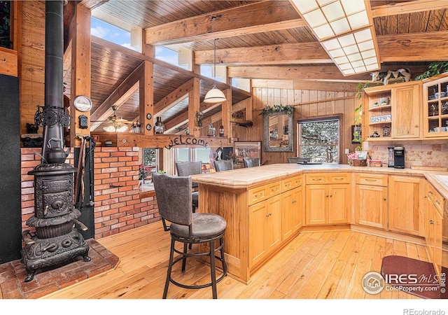 kitchen featuring light brown cabinets, a wood stove, light hardwood / wood-style flooring, tile counters, and beam ceiling