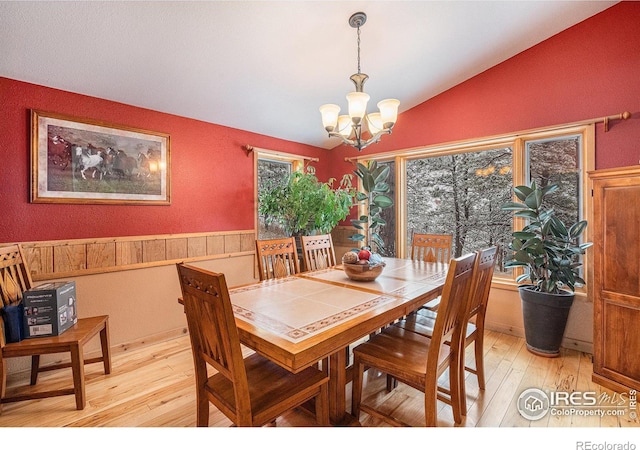 dining space featuring an inviting chandelier, light hardwood / wood-style floors, and vaulted ceiling