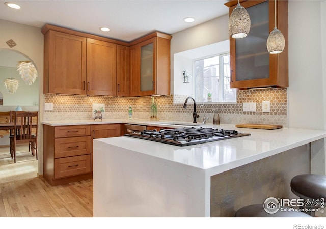 kitchen with a kitchen bar, kitchen peninsula, sink, pendant lighting, and light hardwood / wood-style flooring