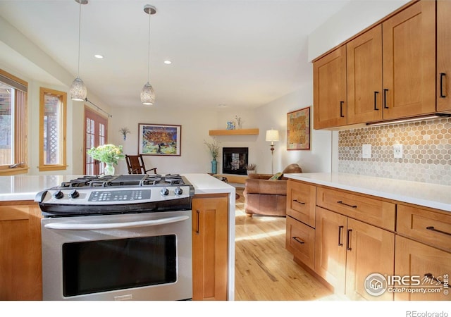 kitchen featuring backsplash, stainless steel gas stove, light hardwood / wood-style floors, and decorative light fixtures