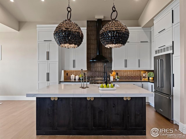 kitchen featuring backsplash, high quality fridge, a center island with sink, and white cabinets