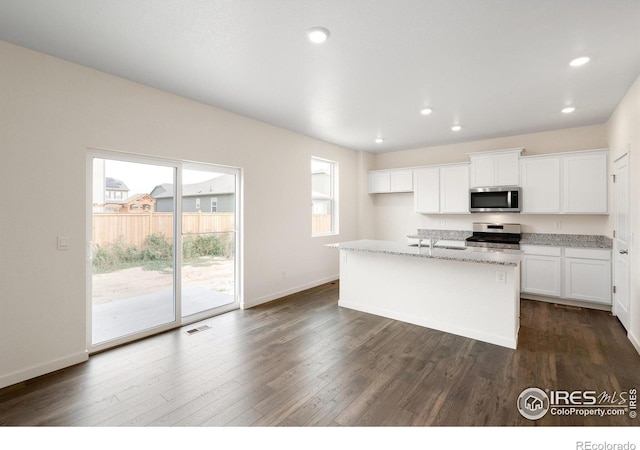 kitchen with light stone countertops, stainless steel appliances, a center island with sink, white cabinets, and dark hardwood / wood-style floors