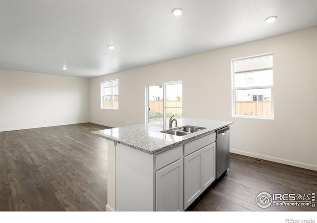 kitchen with white cabinets, light stone counters, sink, dishwasher, and an island with sink