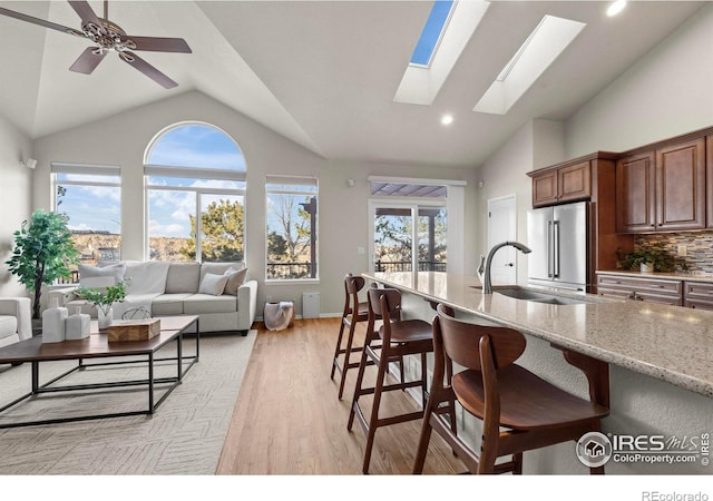 kitchen with a skylight, sink, light stone counters, backsplash, and high end fridge