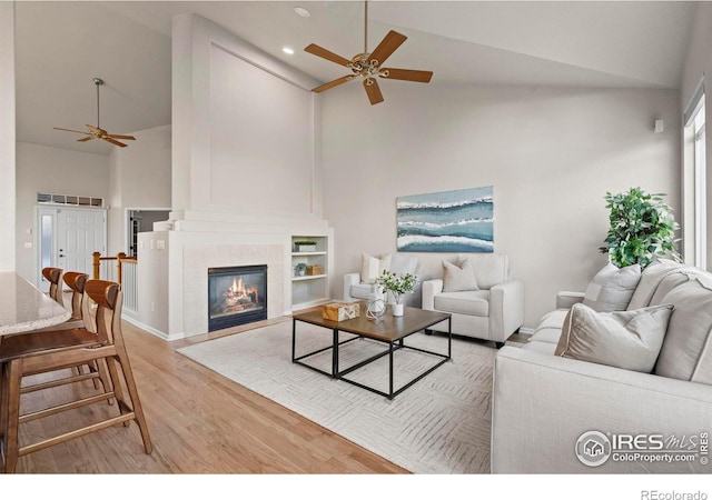 living room featuring ceiling fan, light hardwood / wood-style floors, a fireplace, and high vaulted ceiling