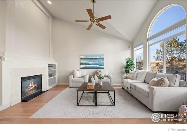 living room with hardwood / wood-style flooring, ceiling fan, a fireplace, and high vaulted ceiling