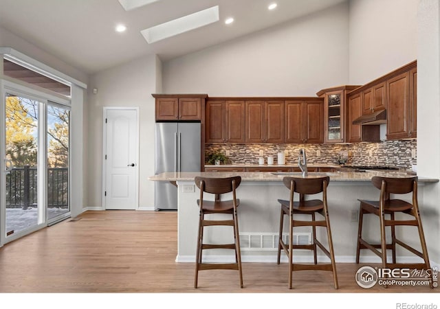 kitchen featuring a skylight, stainless steel fridge, high vaulted ceiling, and light stone countertops