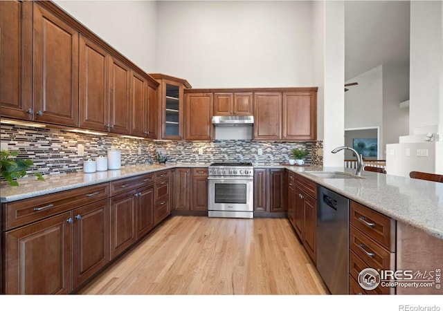 kitchen featuring a high ceiling, sink, appliances with stainless steel finishes, light hardwood / wood-style floors, and light stone counters