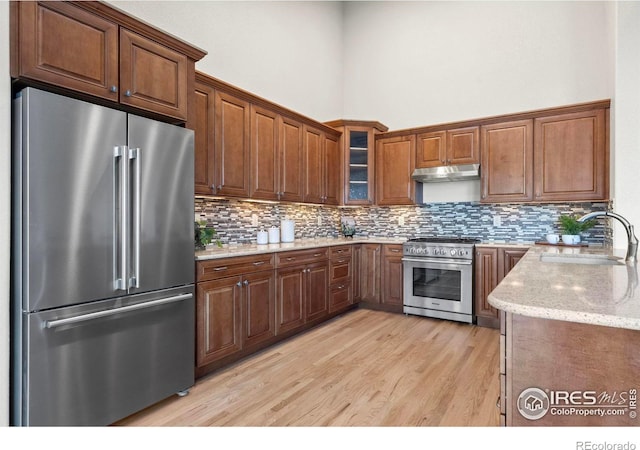 kitchen featuring light stone countertops, sink, a high ceiling, light hardwood / wood-style flooring, and high end appliances