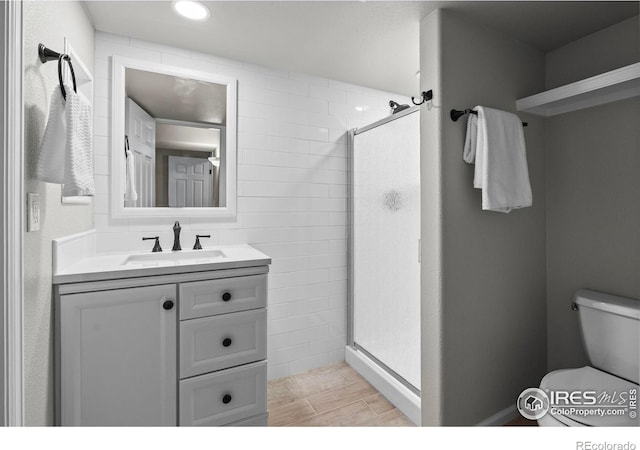 bathroom featuring a shower with door, vanity, and toilet