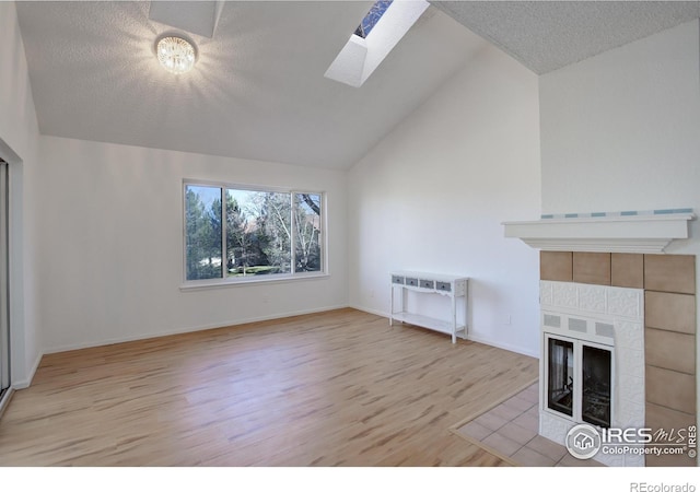 unfurnished living room with a tile fireplace, light hardwood / wood-style flooring, high vaulted ceiling, and a skylight