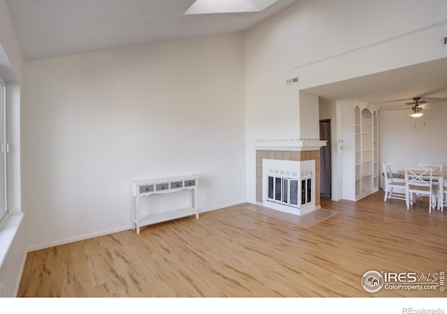 unfurnished living room featuring a tiled fireplace, ceiling fan, and hardwood / wood-style flooring