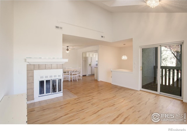 unfurnished living room with a fireplace, a high ceiling, ceiling fan, and hardwood / wood-style floors