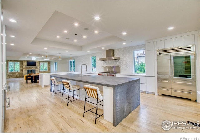 kitchen featuring a fireplace, wall chimney range hood, a tray ceiling, white cabinetry, and a large island