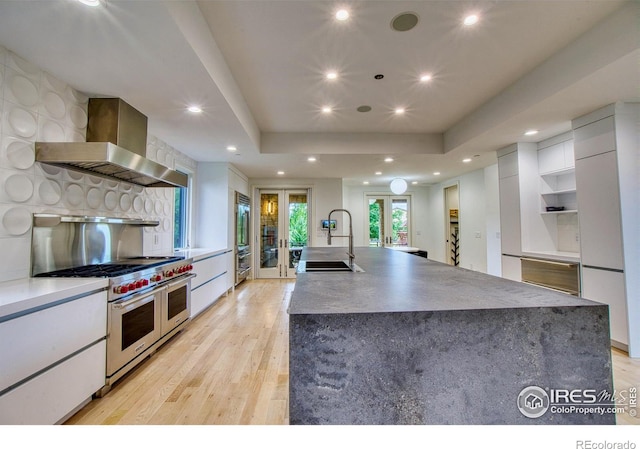 kitchen featuring range with two ovens, french doors, wall chimney exhaust hood, white cabinets, and sink