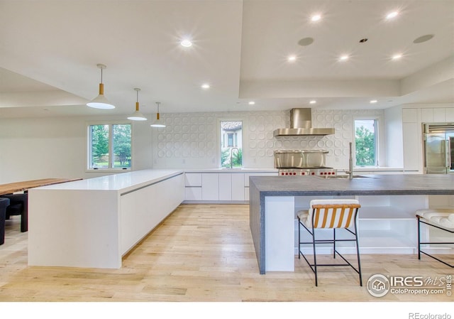 kitchen featuring white cabinetry, stainless steel built in fridge, decorative light fixtures, wall chimney range hood, and sink