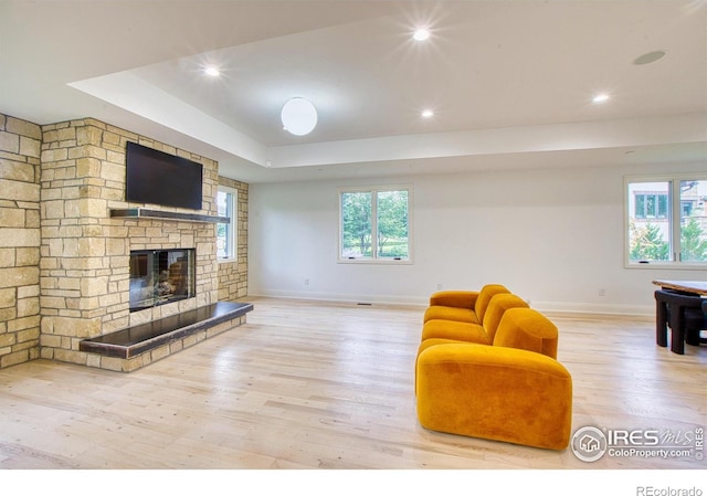 living room with a fireplace, a tray ceiling, and light hardwood / wood-style floors