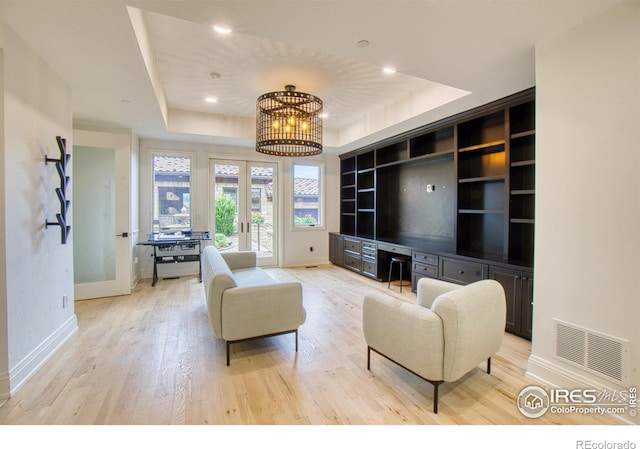 living room featuring a tray ceiling, built in features, french doors, a chandelier, and light hardwood / wood-style flooring