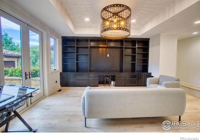 living room with a notable chandelier, a raised ceiling, light hardwood / wood-style flooring, built in features, and french doors