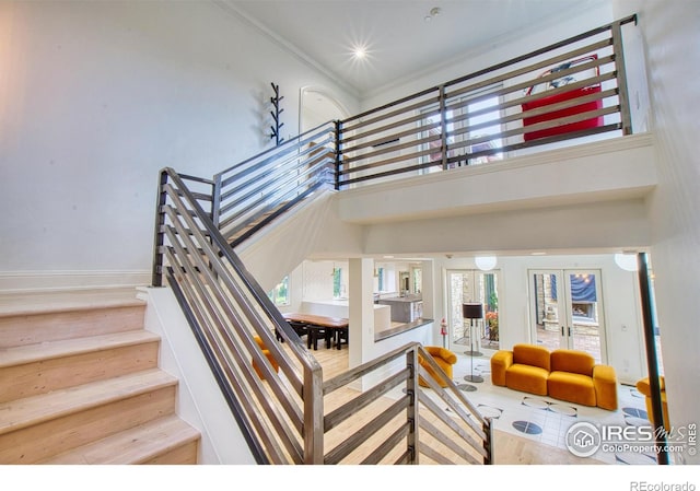 stairway featuring french doors, ornamental molding, and a high ceiling