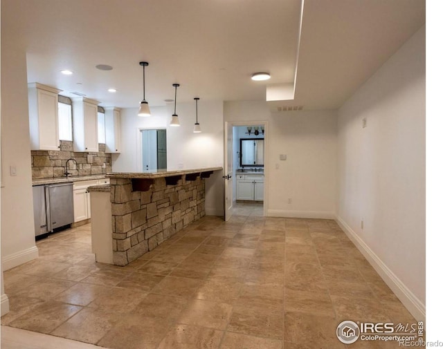 kitchen with tasteful backsplash, decorative light fixtures, stainless steel dishwasher, white cabinets, and a breakfast bar