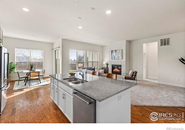 kitchen with appliances with stainless steel finishes, sink, an island with sink, white cabinetry, and a tiled fireplace