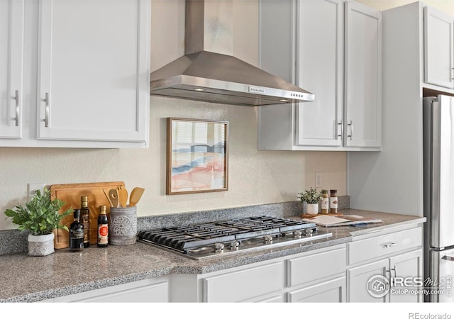 kitchen with light stone countertops, stainless steel appliances, white cabinetry, and wall chimney range hood