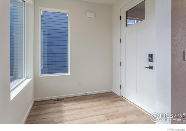 foyer entrance with baseboards, a healthy amount of sunlight, visible vents, and light wood-style floors