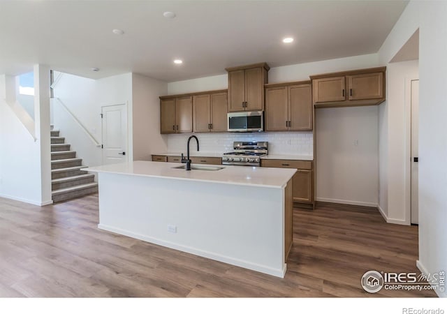 kitchen featuring wood finished floors, appliances with stainless steel finishes, a sink, and decorative backsplash