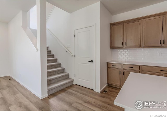 kitchen with tasteful backsplash, light wood-type flooring, light countertops, and baseboards