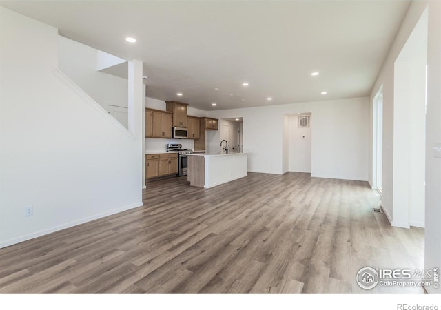 unfurnished living room featuring baseboards, a sink, light wood-style flooring, and recessed lighting