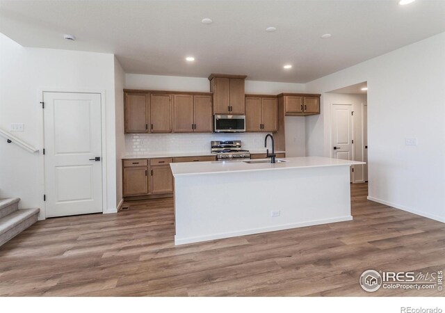 kitchen featuring appliances with stainless steel finishes, light wood-type flooring, a sink, and an island with sink