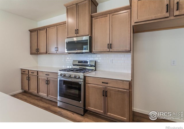 kitchen with stainless steel appliances, baseboards, light countertops, decorative backsplash, and dark wood finished floors