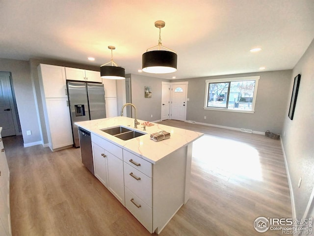 kitchen with sink, decorative light fixtures, white cabinetry, light stone countertops, and a center island with sink