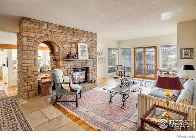 living room featuring a stone fireplace, ornate columns, and a textured ceiling