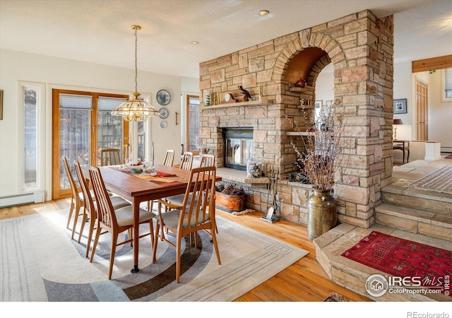 dining room with decorative columns, a stone fireplace, light hardwood / wood-style flooring, and a notable chandelier