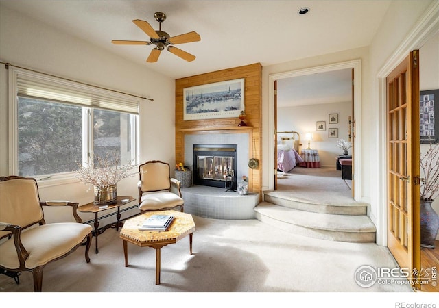 living area with a fireplace, carpet floors, baseboard heating, and ceiling fan