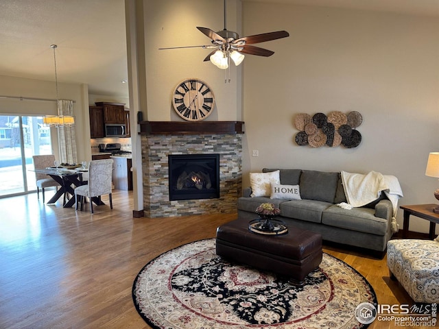 living room with a stone fireplace, ceiling fan, and light hardwood / wood-style floors