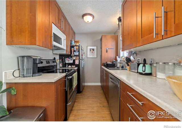 kitchen featuring sink, stainless steel appliances, a textured ceiling, and light wood-type flooring