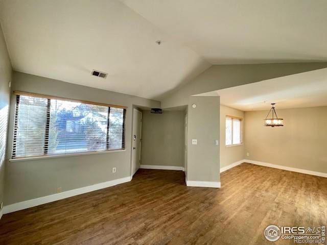 empty room with lofted ceiling, dark wood-type flooring, and a notable chandelier