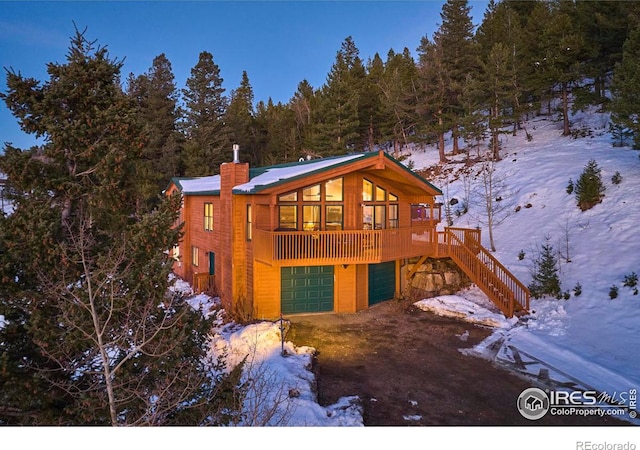 snow covered rear of property with a garage and a wooden deck