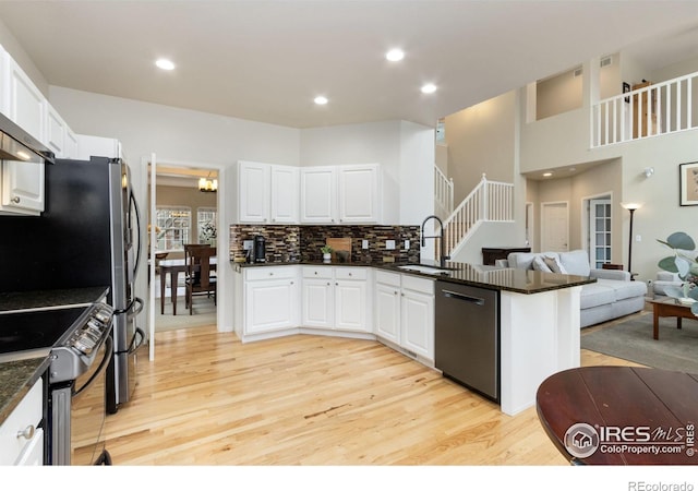 kitchen with sink, kitchen peninsula, appliances with stainless steel finishes, white cabinets, and light wood-type flooring